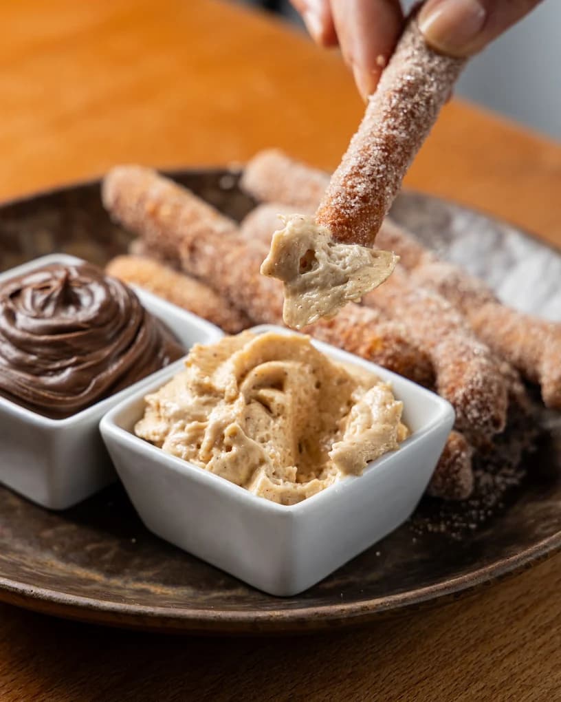 Churros polvilhados com açúcar, a serem mergulhados em creme de doce e chocolate