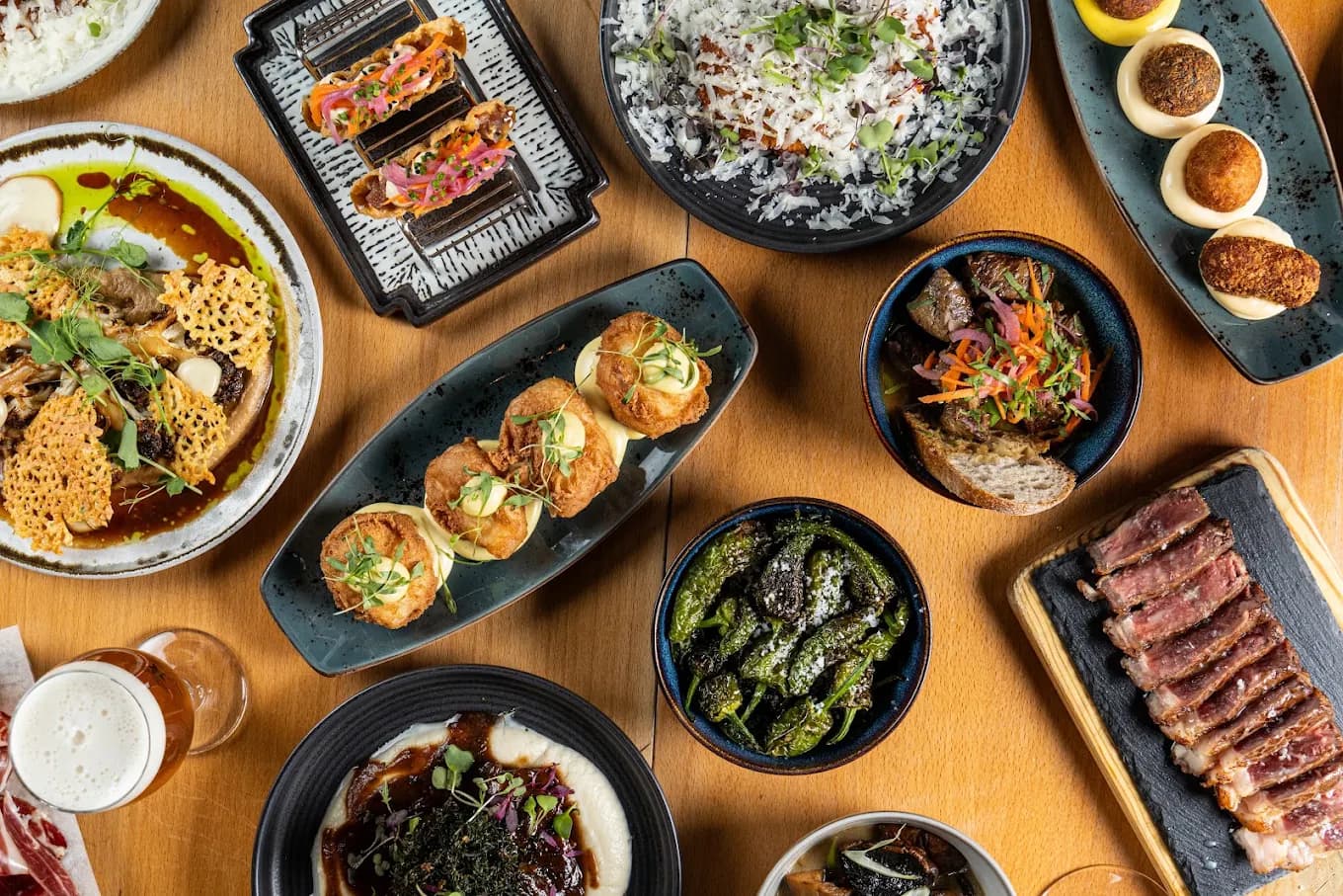Mesa cheia de petiscos para partilhar: croquetes, pimentos padrón, entrecosto e tártaro