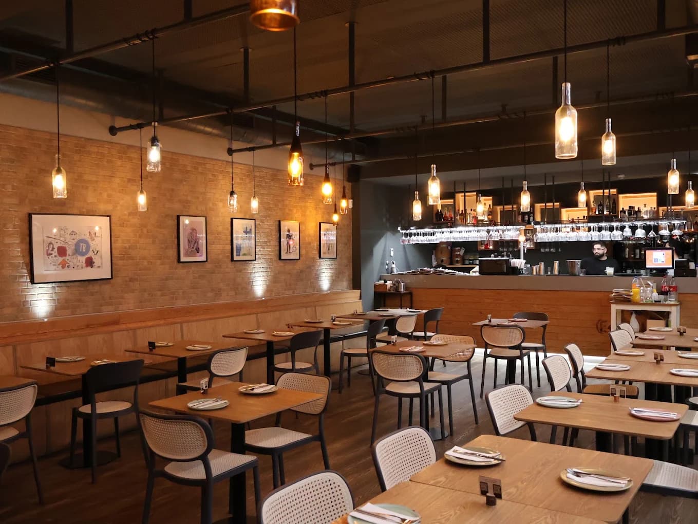 Sala interior do Tapa Bucho, com parede de tijolo, candeeiros suspensos e balcão de bebidas